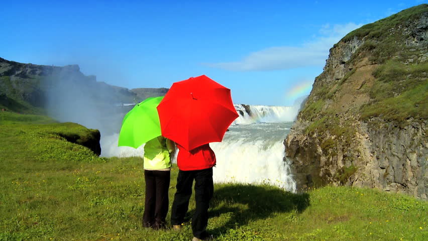 Concept shot of two people by a glacial waterfall using umbrellas to shelter from the economic & environmental climate 60 FPS