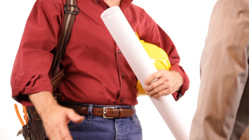 A builder wearing a tool belt, holding a hardhat and set of plans shakes hands with a female client.