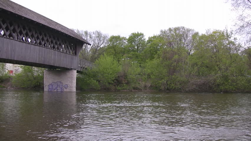 A pan along the length of a wooden covered walking bridge, shot from the river below.  Guelph, Ontario, Canada