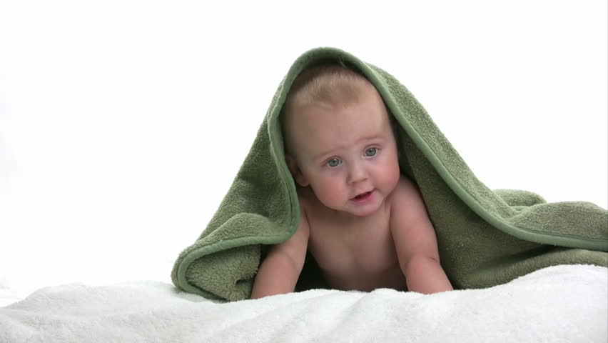 Baby laying on a white towel with a green blanket playing, isolated on white background
