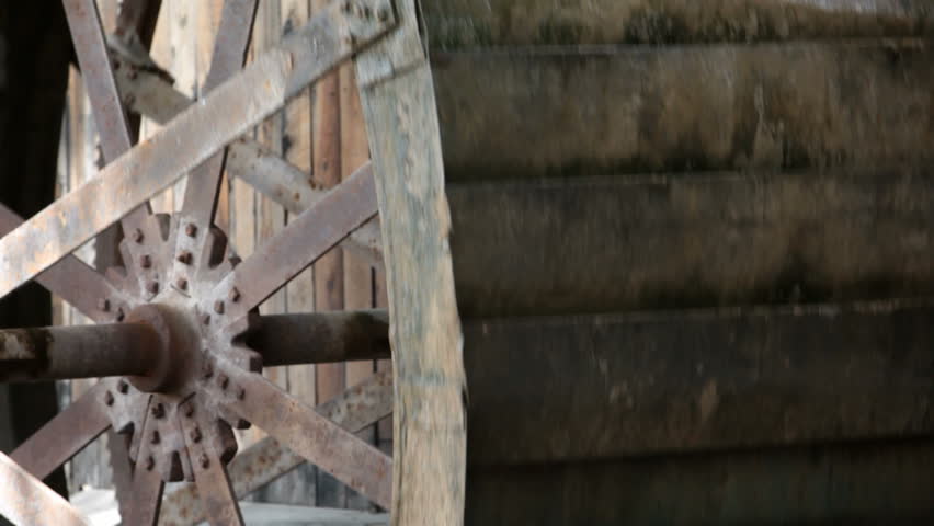 Close up of an old antique water wheel turning against a wood building. Steel wheel and spokes. Turning from power of a small creek in central Utah. Used for a mill.