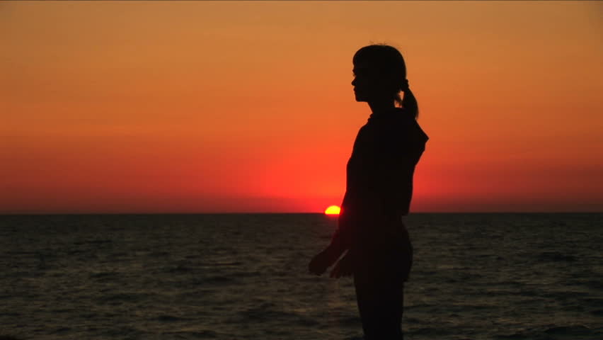 Girl does gymnastics against the sea during a sunset. 