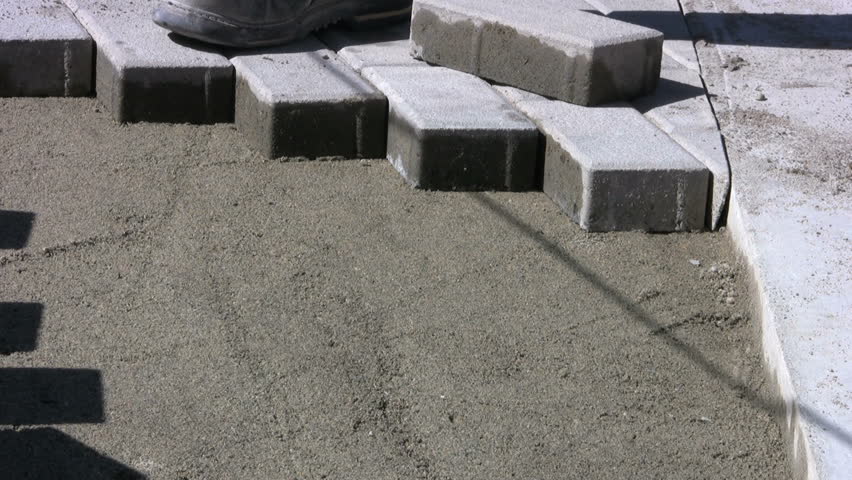 A worker patiently installs interlocking sidewalk bricks on a sunny day. 