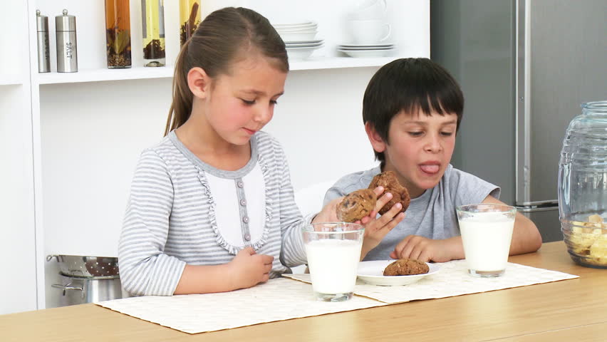 Little brother and sister eating biscuits with milk in the kitchen at home. Footage in high definition
