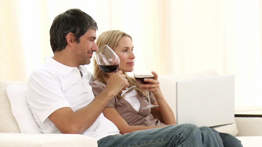 Man and woman using a laptop and drinking wine on sofa at home. Pleasure and computer concepts. Footage in high definition 