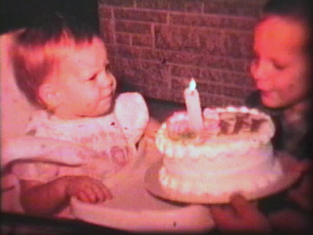 A little girl celebrates her first birthday and sticks her hand in the cake. (Vintage 8mm film)