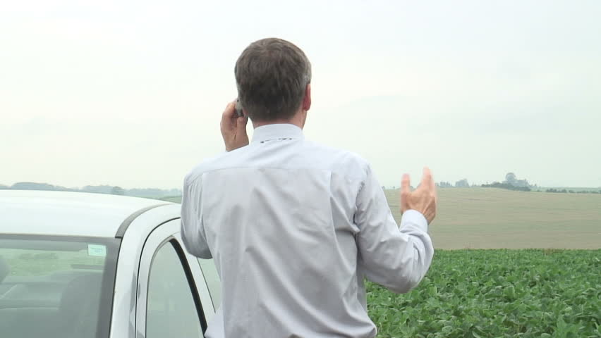 HD 1080i: Annoyed businessman talking on cell phone beside his car.