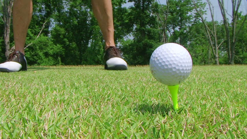 Close-up of golfer getting into stance and teeing off with driver. 