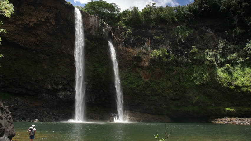 A hiker admiring Wailua Falls on Kauai, Hawaii, as seen from near the bottom of the falls.