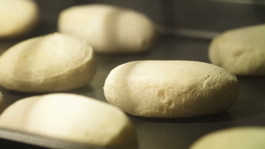 A timelapse of biscuits baking on a cookie sheet in an oven; shallow focus on one biscuit. (Note: The cookie sheet "moves" due to expansion from the heat.)
