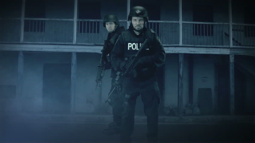 SWAT members in full uniform advancing in dark urban scene.	