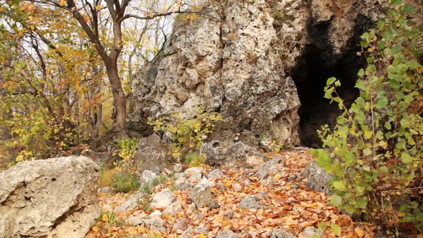 daddy with daughter come into rocky cave among trees in autumn 