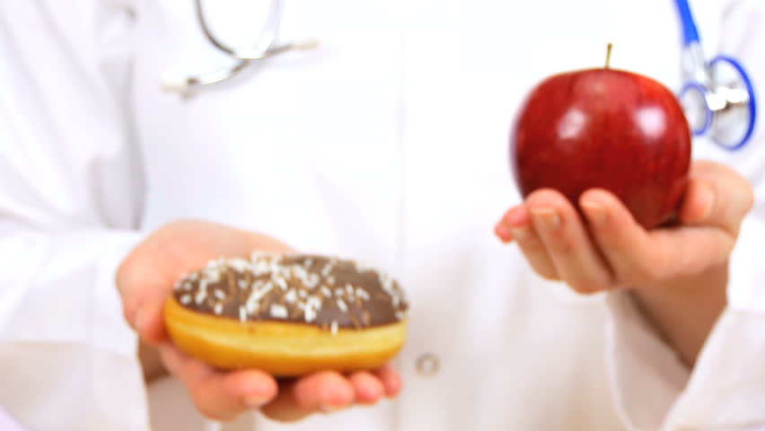 Doctor in white coat weighing up the choice between fresh fruit or sugary doughnut as a healthy food option