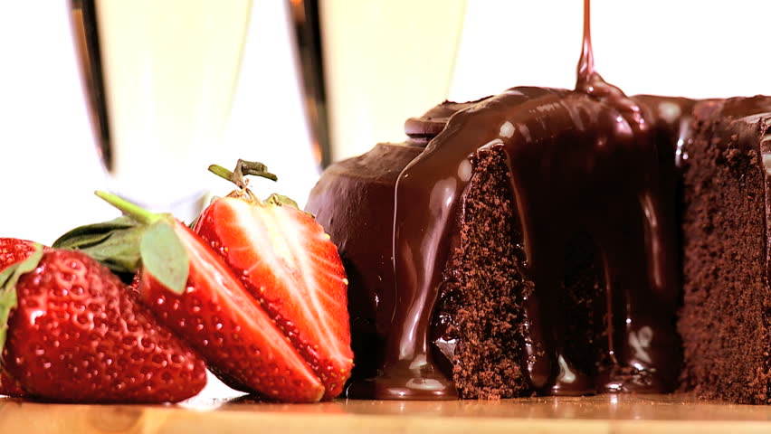 Sticky chocolate cake being covered in sauce while served with fresh strawberries & sparkling white wine