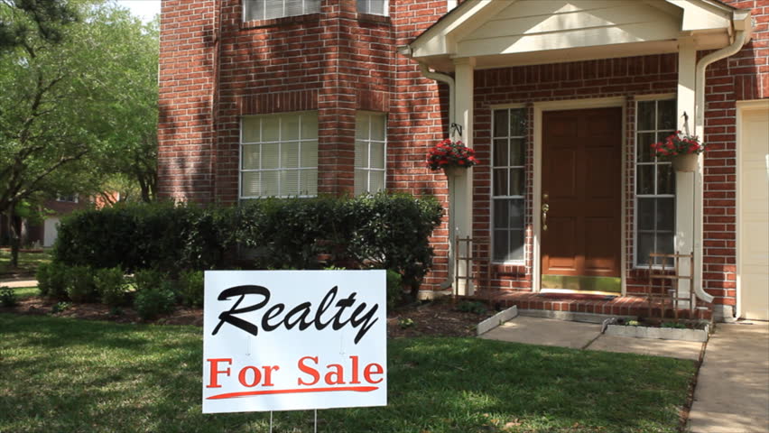A pleased realtor adds SOLD to a for sale sign that is in front of a large home.