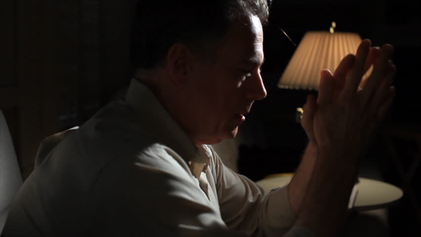 A man sitting in a dimly lit room, who appears worried.