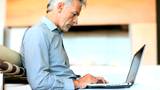 Closeup of mature man using laptop while drinking coffee at home