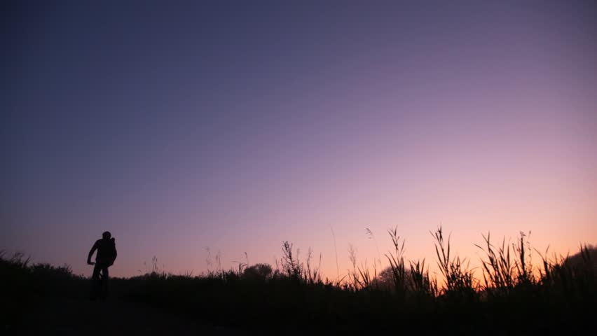 bicyclist rides uphill against summer sunset sky, then rides back 
