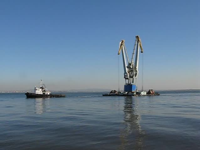 Towboat pulling large crane in port