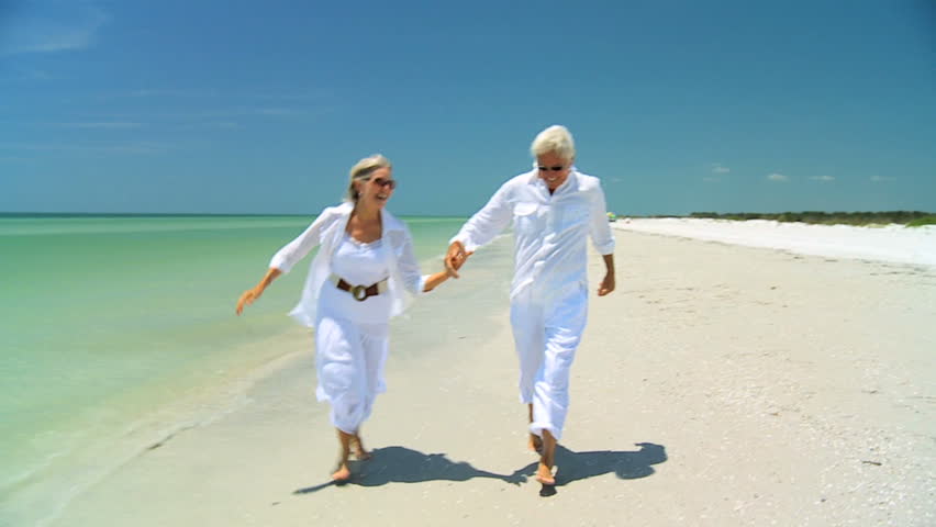 Attractive senior carefree couple running along the beach barefoot enjoying a fun lifestyle 60FPS