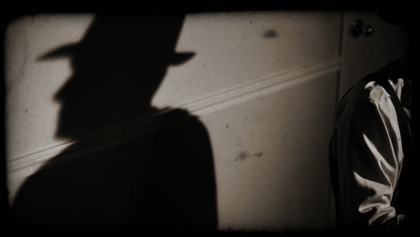 The camera pans from a stark shadow of a person to a man wearing a fedora and typing on a vintage 40s typewriter. Film Noir, old film effect