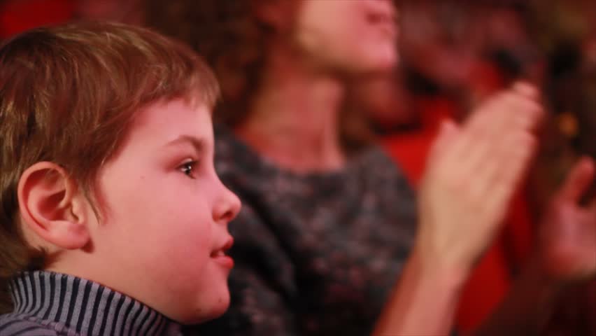 Impressionable little boy sits on a red chair in auditorium of circus and watches a show 