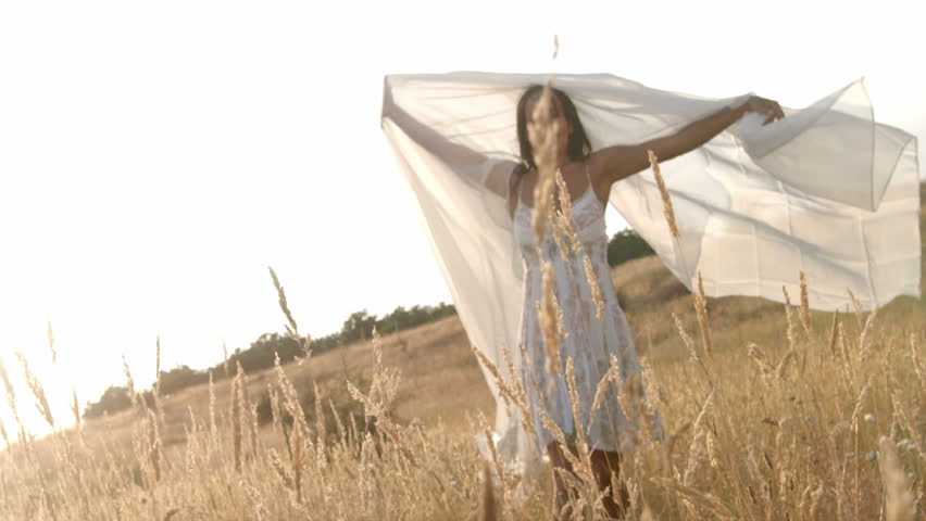 A woman waves a sheer white sheet while moving around a wheat field.