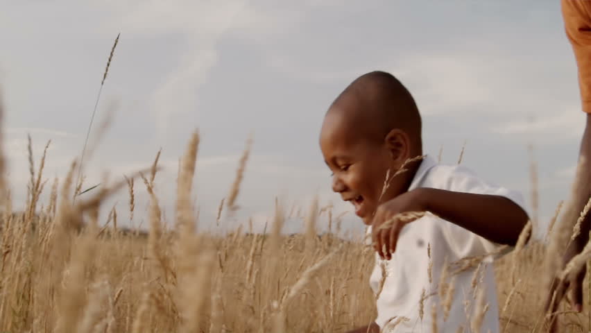 A father and son play in a wheat field on a sunny day.