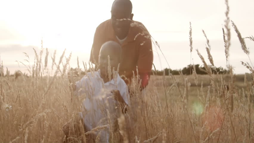 A father and son play in a wheat field on a sunny day.