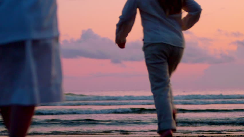 Three children and two adults run toward toward the sunset and jump on the beach.