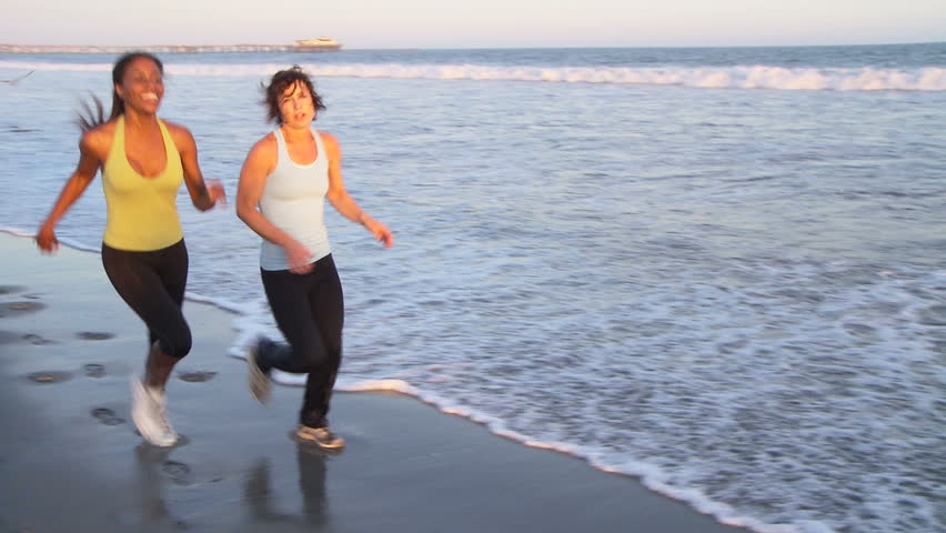 Two young women catching their breath at end of run on the beach 