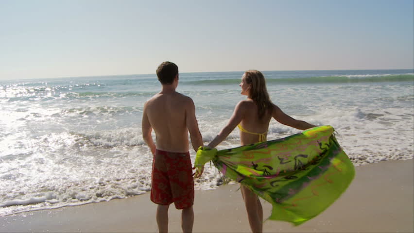 Young couple kissing at ocean's edge with scarf blowing in breeze