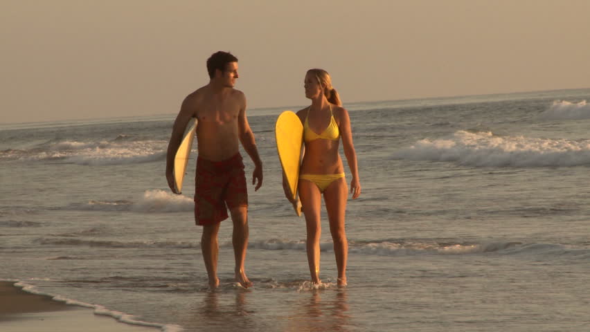 Young couple walking out of waves with surfboards