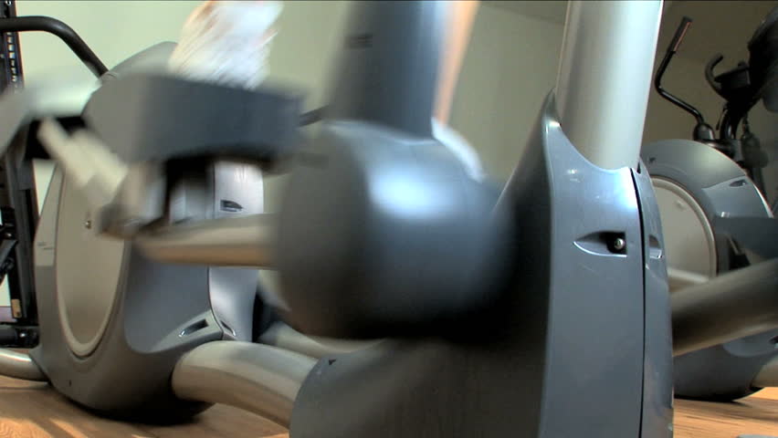 Close-up legs & feet working an exercise machine at a gym