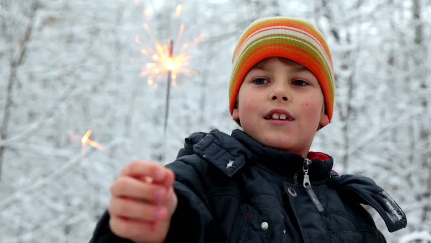 Boy in orange hat playing with sparklers in snow forest