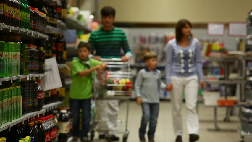 A family of four walking along the beverage row in the supermarket, the sons putting drinks into the trolley