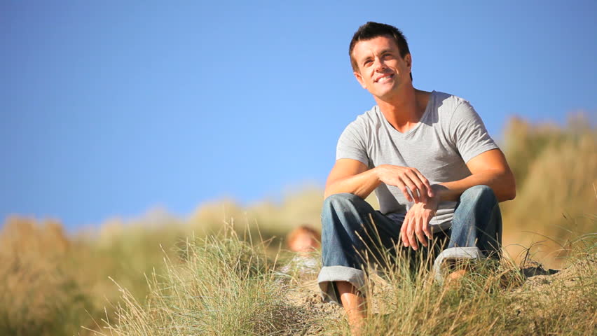 Adorable little blond boy & his young father enjoying time together  sitting in sand dunes by the coast