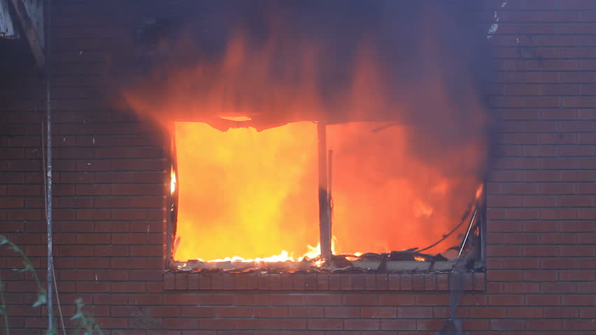 Fire burns intense house burning with flames and smoke coming through broken window.