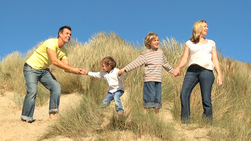 Attractive young caucasian family enjoying leisure time together on coastal sand dunes  filmed at 60FPS