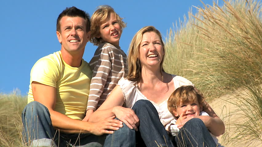 Attractive young caucasian family enjoying outdoor time together on coastal sand dunes  filmed at 60FPS