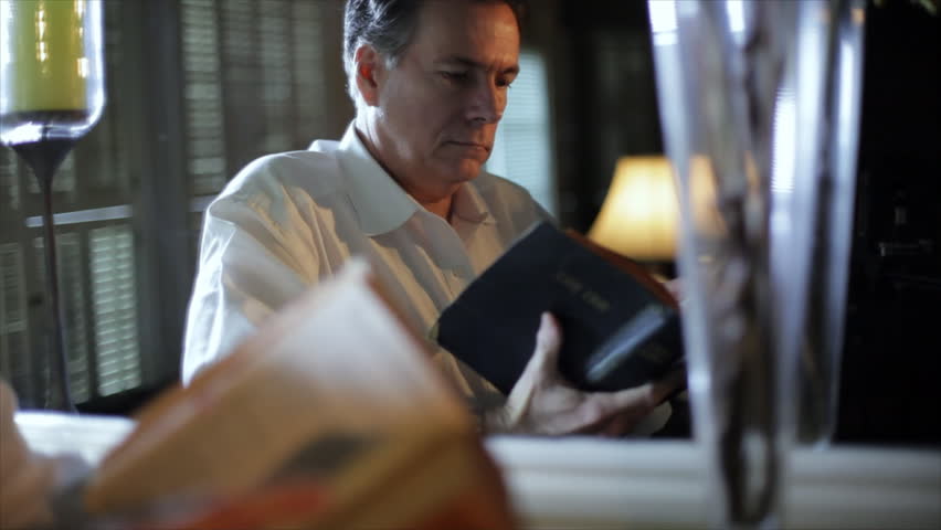 A manÃÂ¢??s image is reflected in a mirror as he reads from his Bible then contemplates what he has read. Dolly shot, movement to the left.