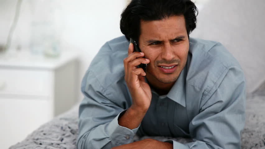 Frustrated man on the phone on the bed in a bed room