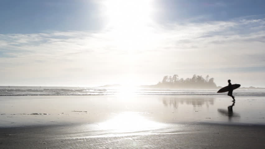 Surfer runs across beach. Silhouette of surfer running with surfboard. Reflection in the sand. Tofino, British Columbia, Canada. 