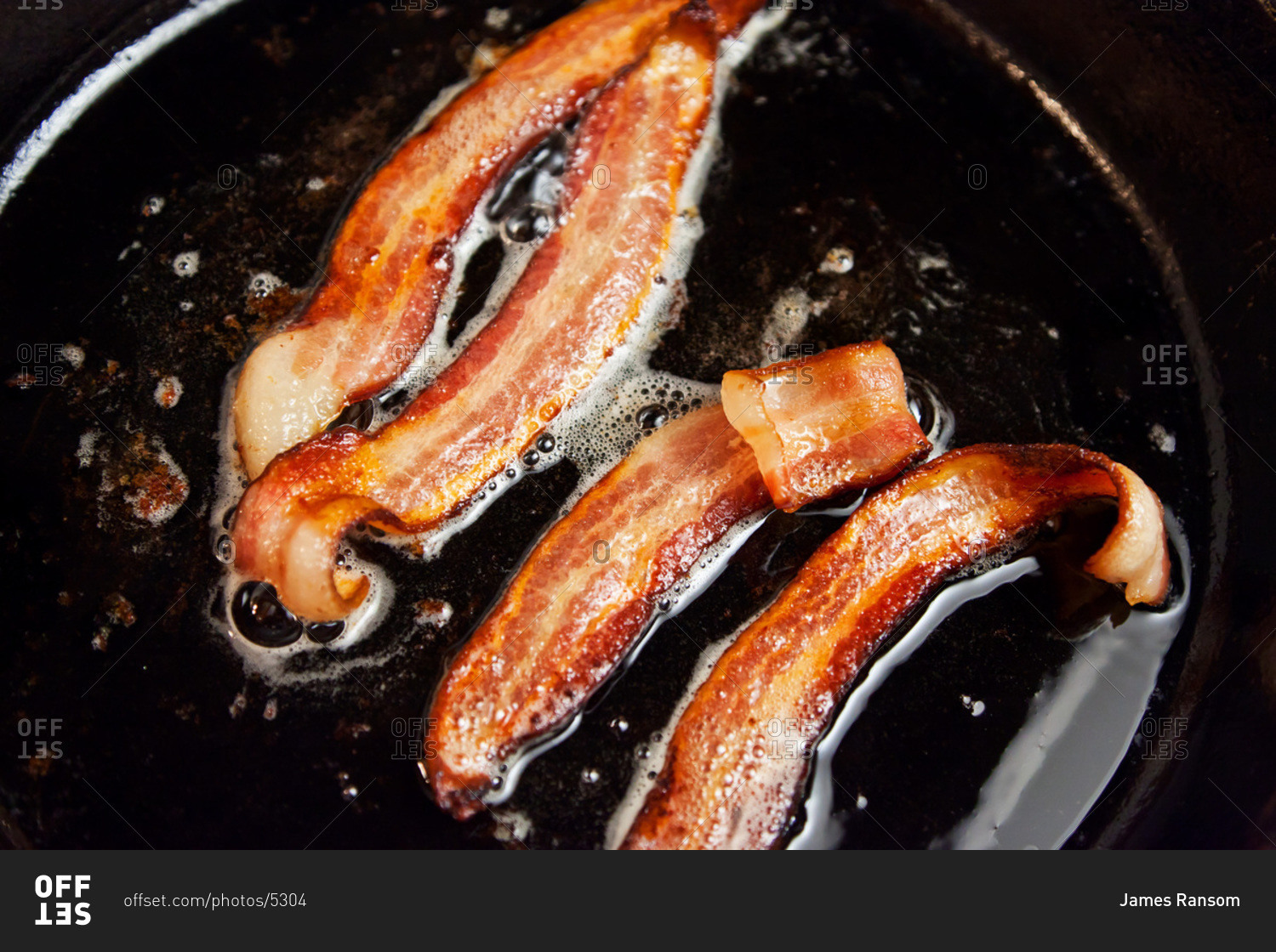 Four pieces of bacon frying in a cast iron skillet