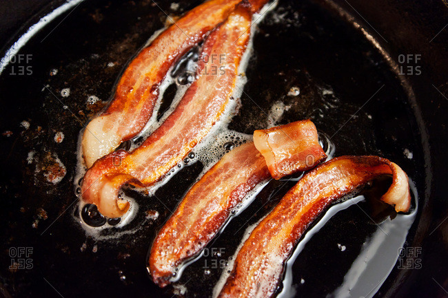 Bacon frying in stove top pan. Sizzling bacon strips in silver skillet.  Stock Photo