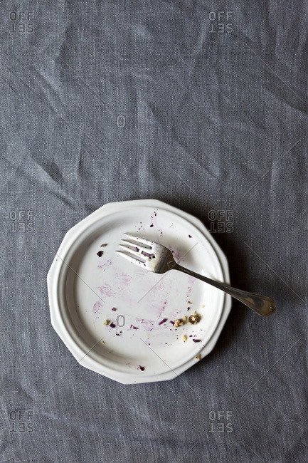 An empty plate with a fork on a gray table cloth