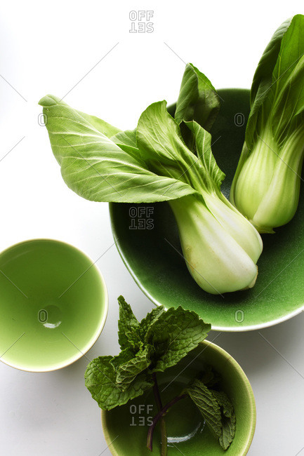 Still life of bok choy, mint in three green bowls on white surface