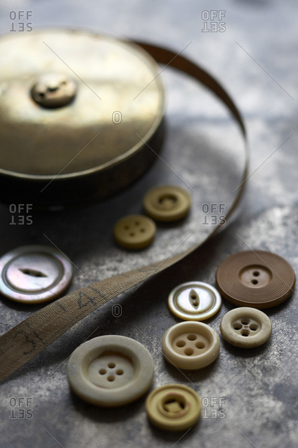 Still life of buttons and old, vintage brass measuring tape on metal surface