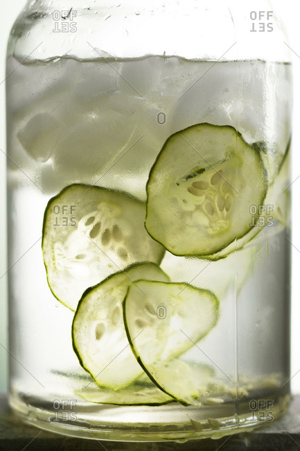Glass jar filled with sliced cucumbers, water and ice cubes