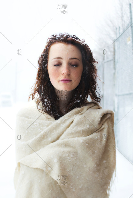Young girl wrapped in beige pashmina shawl in snowstorm.  Hair covered in snow flakes.